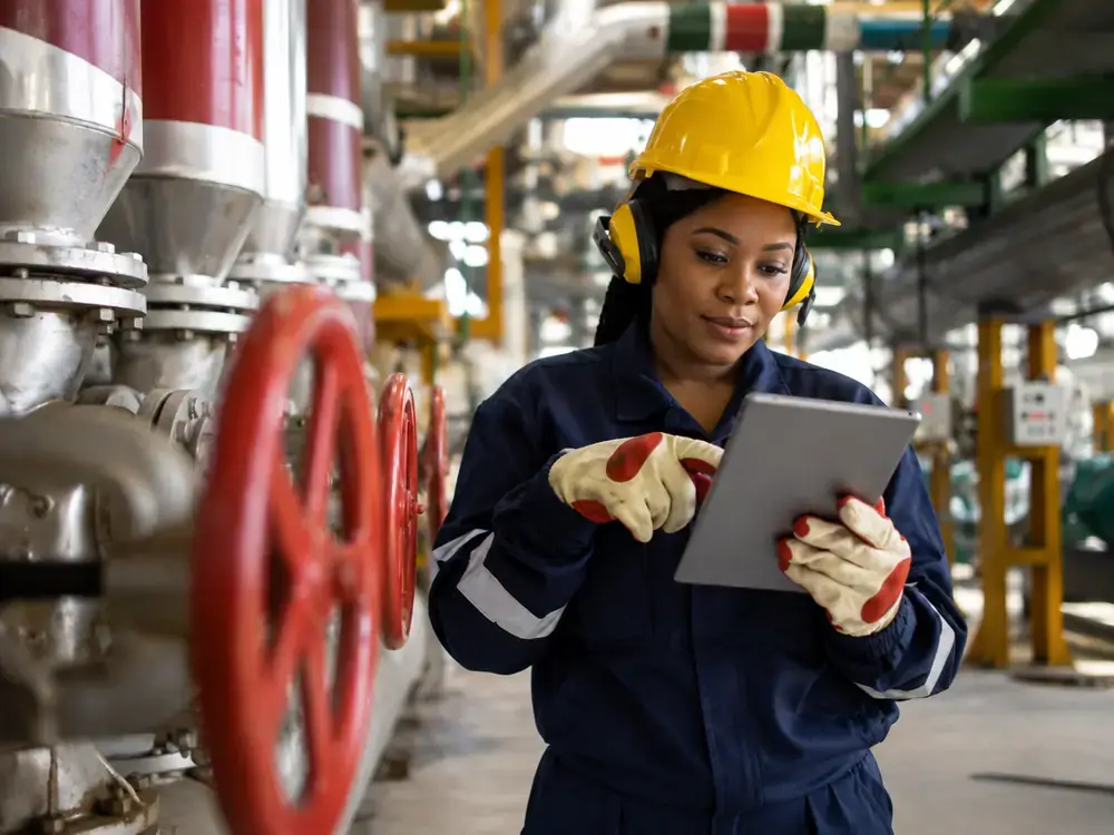 Engineer in a hard hat reviewing procurement data on a tablet in an industrial facility