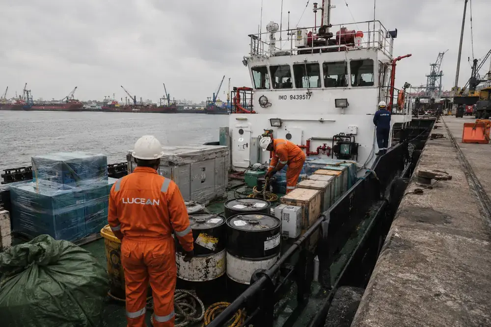 Crew loading drums, crates and pallets of stores onto a vessel at the quayside